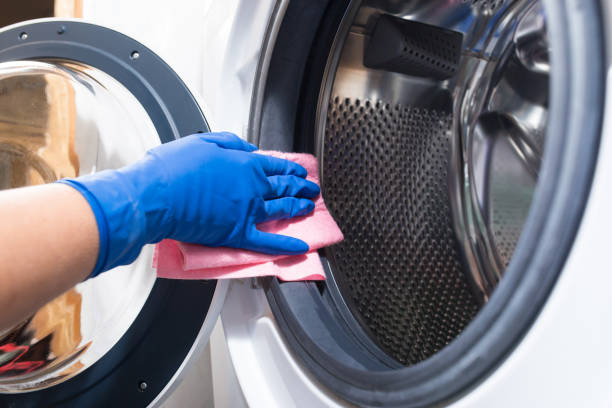 A gloved hand cleaning the inside of a washing machine with a pink cloth for maintaining fresh clothes and linens.