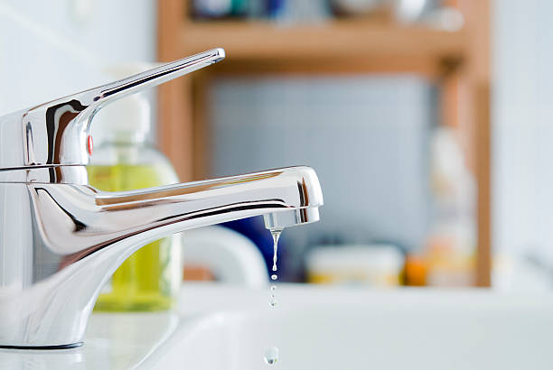 A shiny bathroom faucet drips water, illustrating a need for effective cleaning techniques for spotless surfaces.