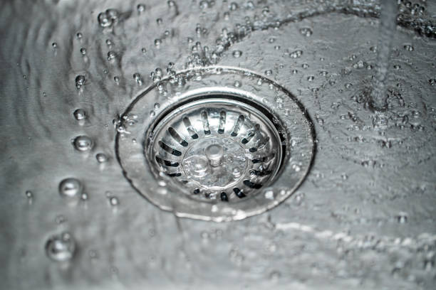 Water running over a clean kitchen sink drain with droplets around it.